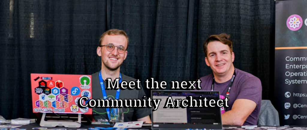 Two men sit behind laptops at a booth with large overlaid text reading, "Meet the next Community Architect". The background consists of black drapes and a partial event banner.